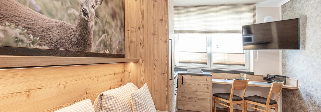 Studios-Giggitenne A modern room with warm wooden elements and a large window.
On the wall hangs a picture of a deer, and there is a television as well as a desk with chairs. - GIGGI Tenne Studios - Sölden