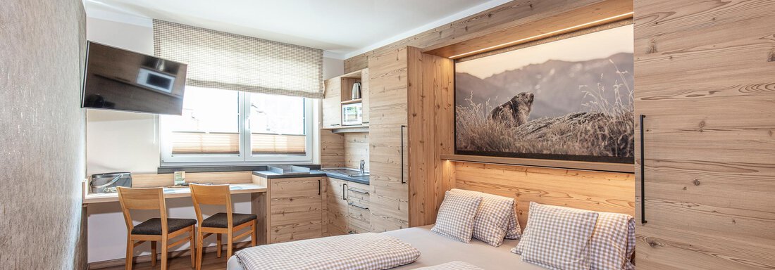A modern room with wooden decor and large windows. It features a double bed, a small kitchenette, and a dining area. - GIGGI Tenne Studios - Sölden