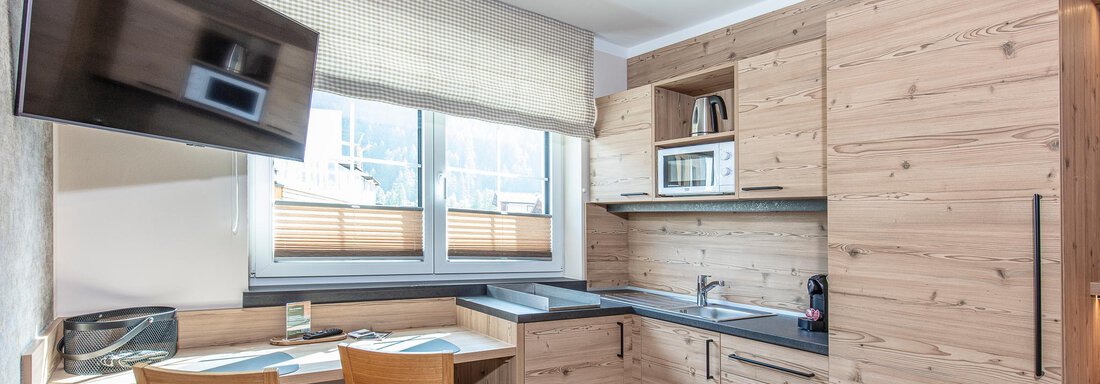 A modern wooden kitchen with a dining table and two chairs. The equipment includes a microwave, a kettle, and a television. - GIGGI Tenne Studios - Sölden