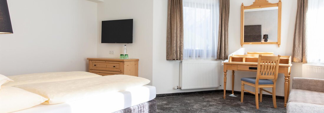 Ein helles Hotelzimmer mit zwei Einzelbetten, einem Schreibtisch und einem Fernseher. Große Fenster lassen viel Licht herein und sorgen für eine freundliche Atmosphäre. - Glanz & Glory Hotel - Sölden