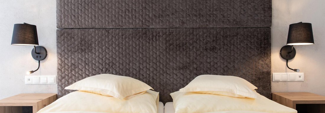 Ein modernes Schlafzimmer mit zwei Betten und einem stilvollen Kopfteil. An beiden Seiten befinden sich Nachttischlampen. - Glanz & Glory Hotel - Sölden
