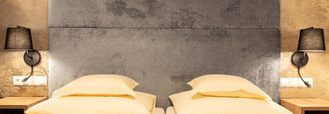 Ein modernes Schlafzimmer mit zwei Einzelbetten und einem eleganten Kopfteil. Die Wände sind mit stilvollem Muster dekoriert und die Beleuchtung sorgt für eine gemütliche Atmosphäre. - Glanz & Glory Hotel - Sölden
