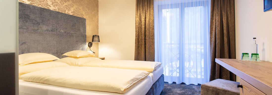 Ein modernes Schlafzimmer mit einem Doppelbett und einem eleganten Design. Große Fenster lassen viel Licht herein und bieten einen Blick nach draußen. - Glanz & Glory Hotel - Sölden