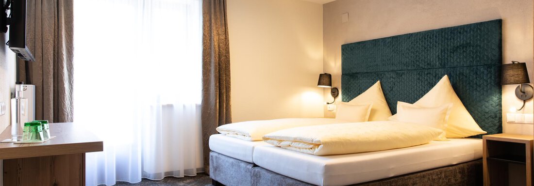 Ein modernes Hotelzimmer mit einem großen Bett und eleganten Kissen. Natürliches Licht strömt durch das Fenster, und es gibt einen Schreibtisch aus Holz. - Glanz & Glory Hotel - Sölden