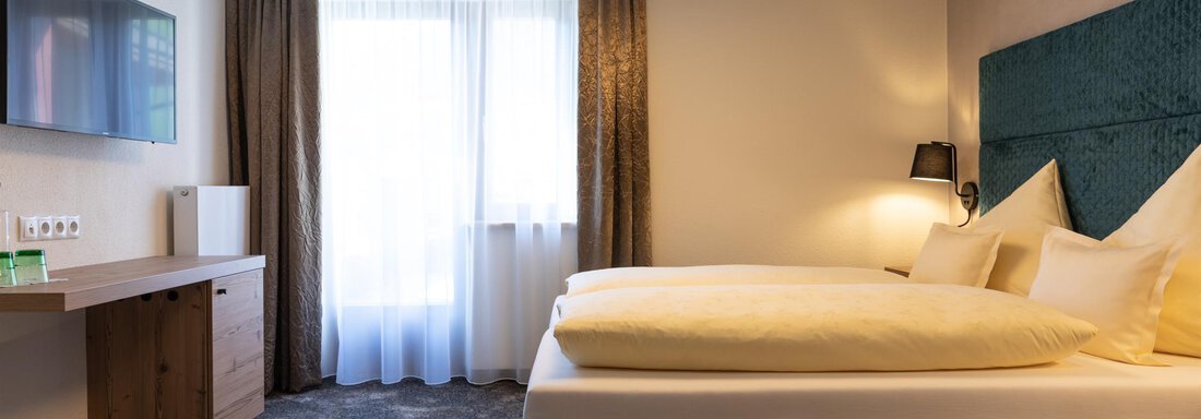 Ein modernes Schlafzimmer mit einem großen Fenster und zwei bequemen Betten. Der Raum ist mit einem Fernseher und stilvollen Möbeln ausgestattet. - Glanz & Glory Hotel - Sölden