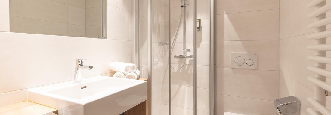 Ein modernes Badezimmer mit einer Dusche, einem Waschbecken und einer Toilette. Helle Fliesen und Holzdetails sorgen für eine einladende Atmosphäre. - Glanz & Glory Hotel - Sölden