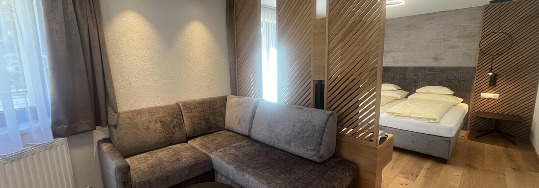 Ein modernes Zimmer mit einer gemütlichen Sitzecke und einem Doppelbett im Hintergrund. Der Boden ist aus Holz und die Wände sind hell gestaltet. - Glanz & Glory Hotel - Sölden