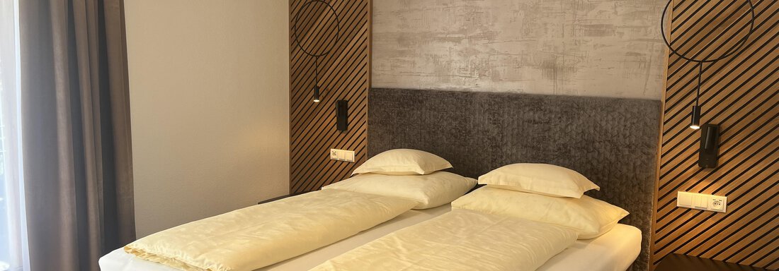 Ein modernes Zimmer mit zwei Einzelbetten und elegantem Holzfußboden. Die Wände sind schlicht gestaltet, und es gibt große Fenster, die Tageslicht hereinlassen. - Glanz & Glory Hotel - Sölden