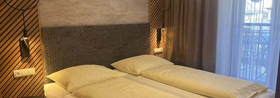 Ein modernes Schlafzimmer mit zwei Einzelbetten und stilvollem Design. Die Wände sind mit Holz und neutralen Farben gestaltet, und es gibt große Fenster für Tageslicht. - Glanz & Glory Hotel - Sölden