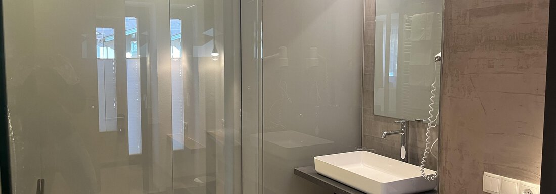 Ein modernes Badezimmer mit einer Glasdusche und einem eleganten Waschbecken. Die Wände sind in dezenten Farben gehalten und es gibt Holzregale für Handtücher. - Glanz & Glory Hotel - Sölden