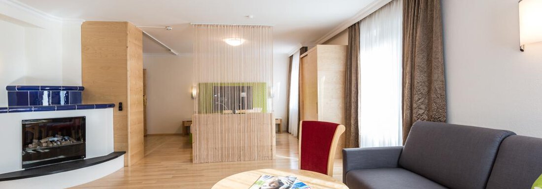Ein modernes Wohnzimmer mit einem gemütlichen Sofa, einem runden Tisch und warmen Holzboden. Große Fenster lassen viel Tageslicht herein und verleihen dem Raum eine einladende Atmosphäre. - Glanz & Glory Hotel - Sölden