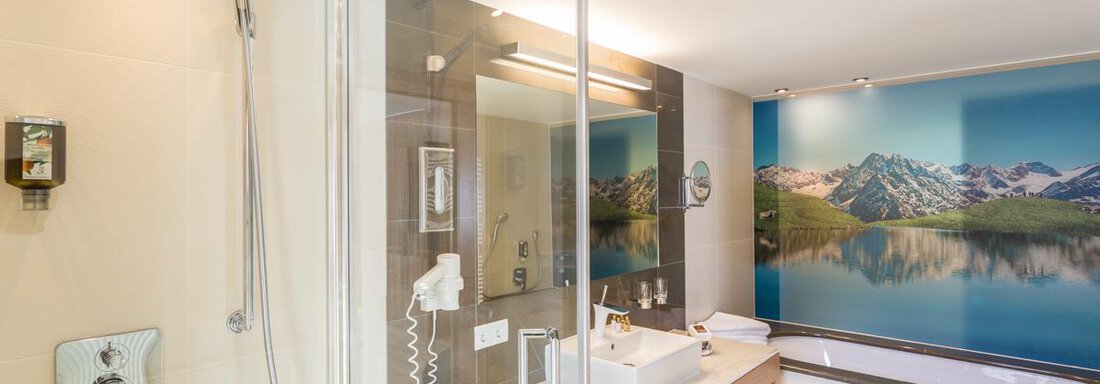Ein modernes Badezimmer mit einer Dusche und einem Waschtisch aus Holz. Im Hintergrund ist ein schönes Bergbild zu sehen. - Glanz & Glory Hotel - Sölden