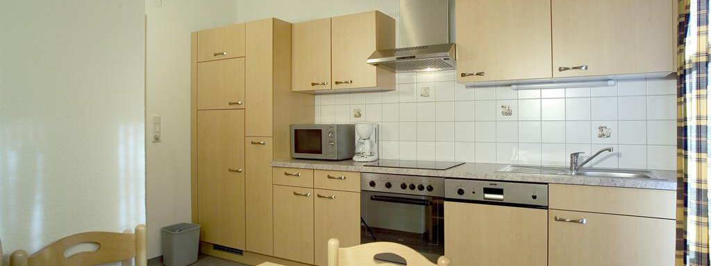 Küche A modern kitchen with light wood cabinets and stainless steel appliances. The table is in the center, surrounded by simple chairs. - Gstrein Andreas - Sölden