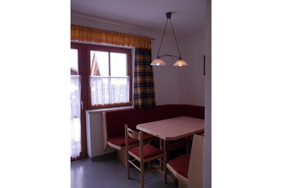 A cozy dining area with a table and chairs. The windows are decorated with curtains, and the walls are in neutral colors. - Gstrein Andreas - Sölden
