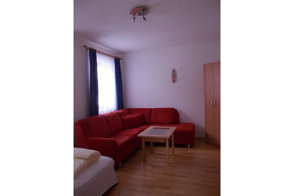 A cozy living space with a red sofa and a small table. Curtains hang at the windows and the floor is made of wood. - Gstrein Andreas - Sölden
