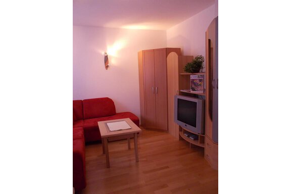 A modern living room with a red sofa and a table. There is a television on the wall and a wooden cabinet. - Gstrein Andreas - Sölden