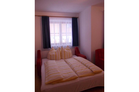 A cozy bedroom with a large bed and red armchairs. The window has bright curtains that let in natural light. - Gstrein Andreas - Sölden