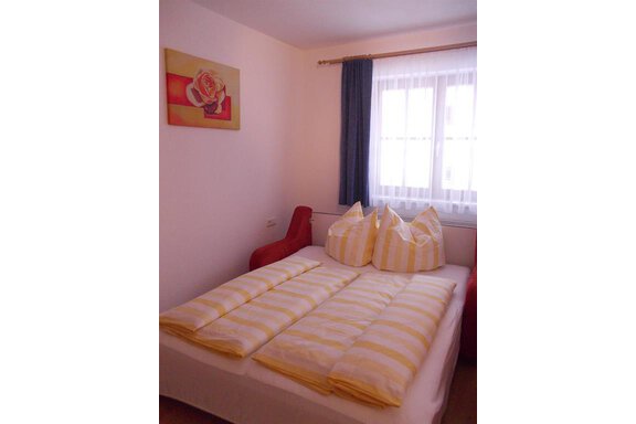 A cozy bedroom with a double bed and yellow-striped pillows. A picture of a rose hangs on the wall, and the room has large windows that let in plenty of light. - Gstrein Andreas - Sölden