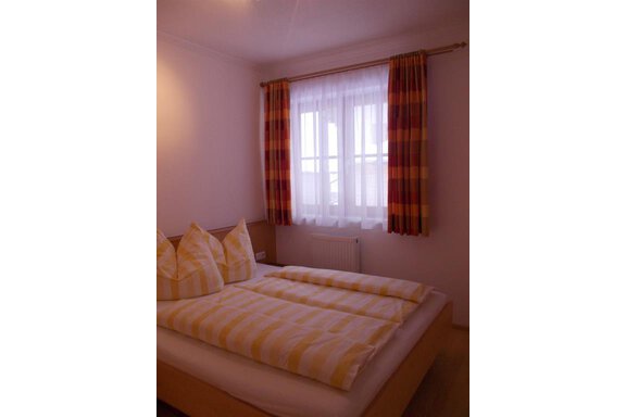 A simple bedroom with a bed that has yellow and white striped bedding. The windows are decorated with bright curtains, allowing plenty of daylight in. - Gstrein Andreas - Sölden