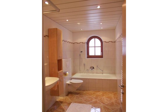 A modern bathroom with a bathtub and shower. It features bright tiles and a large window. - Gstrein Andreas - Sölden