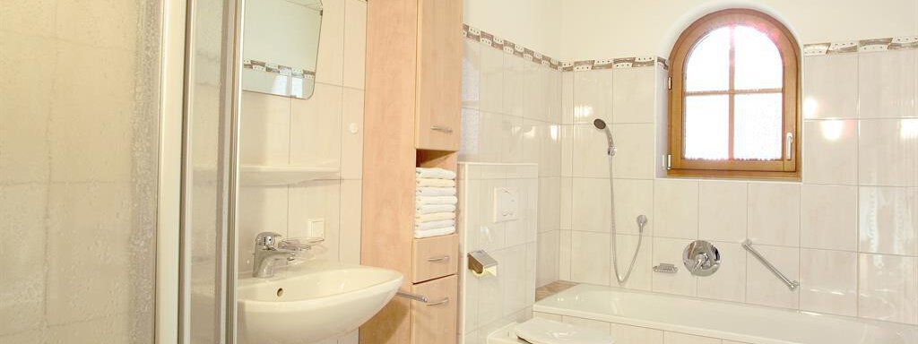 A modern bathroom with a bathtub and a shower. There is a sink with a mirror and a wooden shelf for towels. - Gstrein Andreas - Sölden