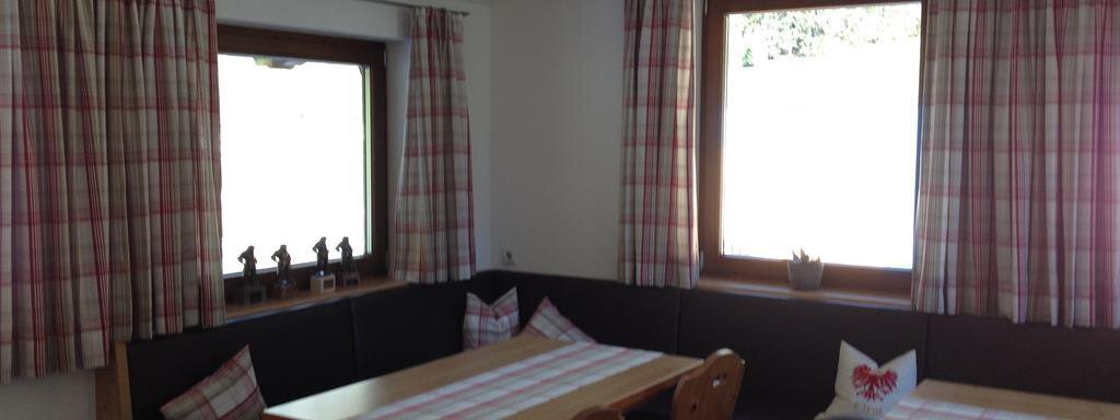 Aufenthaltsraum A cozy room with wooden decor and seating at tables. The windows are adorned with checked curtains, and light streams in. - Haus Almrausch - Sölden