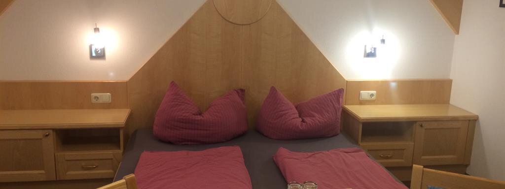A cozy bedroom with a double bed and red pillows. The room is bright and features a wooden desk with chairs. - Haus Almrausch - Sölden