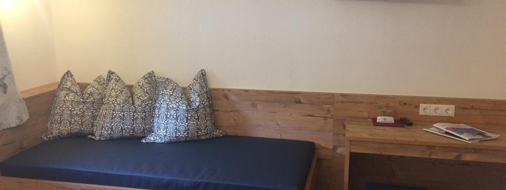 A cozy room with a blue seating area and colorful cushions. A television hangs on the wall, and a small table stands next to it. - Haus Almrausch - Sölden