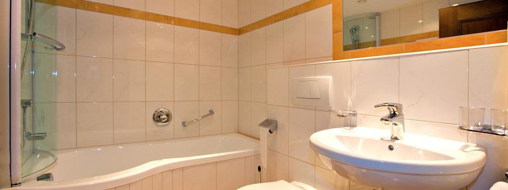 A modern bathroom with a bathtub and a shower. There is a sink and bright tiles. - Haus Almrausch - Sölden