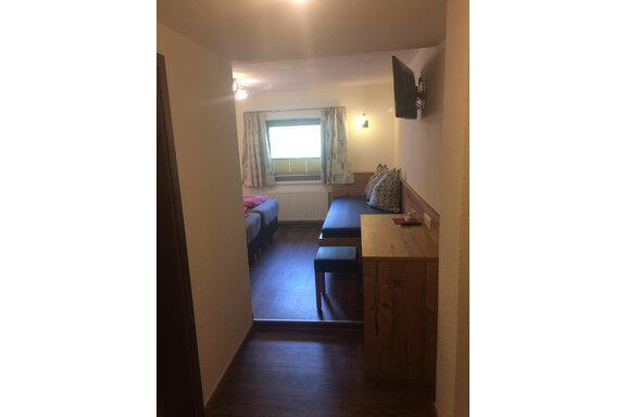 A cozy room with wooden paneling and a table. In the room, there is a window with curtains and a seating area. - Haus Almrausch - Sölden