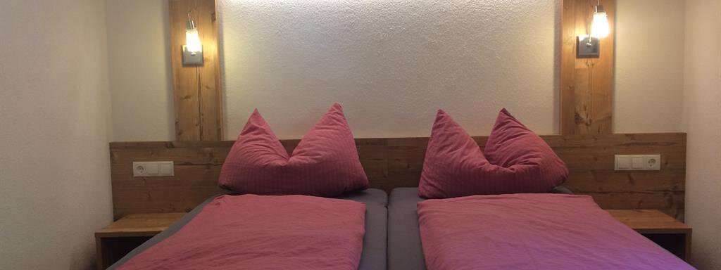 A cozy room with two single beds and red cushions. The walls are in soft colors, with gentle lighting above the beds. - Haus Almrausch - Sölden