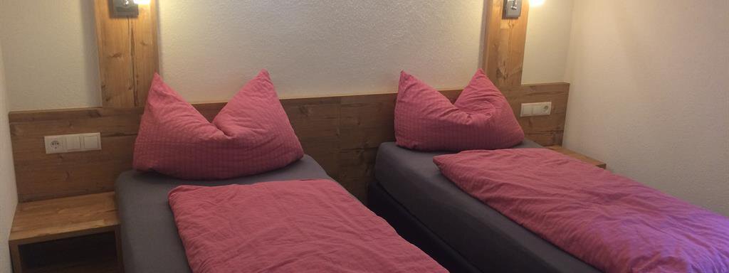 A cozy bedroom with two separate beds and pink bedspreads. The walls are light, and there are wooden paneling and soft lighting. - Haus Almrausch - Sölden