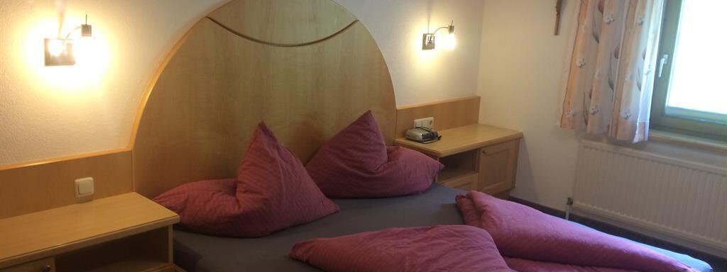 Dreibettzimmer A simple bedroom with a large bed and two big pink pillows. The walls are light, and a window lets in a lot of daylight. - Haus Almrausch - Sölden