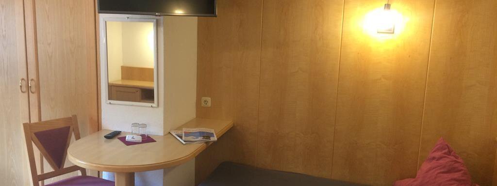 A cozy room with a bed, a table, and a television on the wall. The room has wood-paneled walls and warm lighting. - Haus Almrausch - Sölden