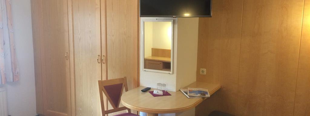 A simple room with a table, a chair, and a bed. A television is hanging on the wall, and there is a wooden wardrobe. - Haus Almrausch - Sölden
