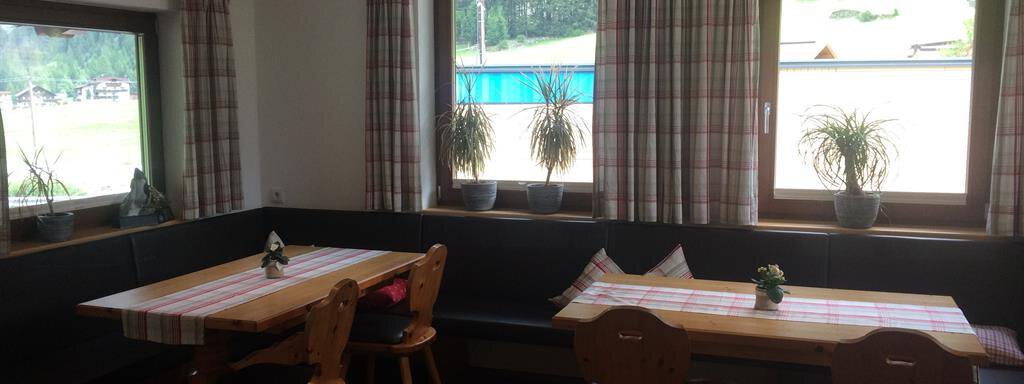 A cozy dining room with wooden chairs and tables. Large windows with plants create a bright atmosphere. - Haus Almrausch - Sölden