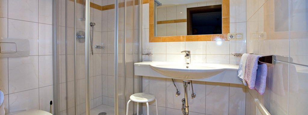 A modern bathroom with a glass shower, a sink, and a mirror. The room features bright tiles and a clean, elegant decor. - Haus Almrausch - Sölden