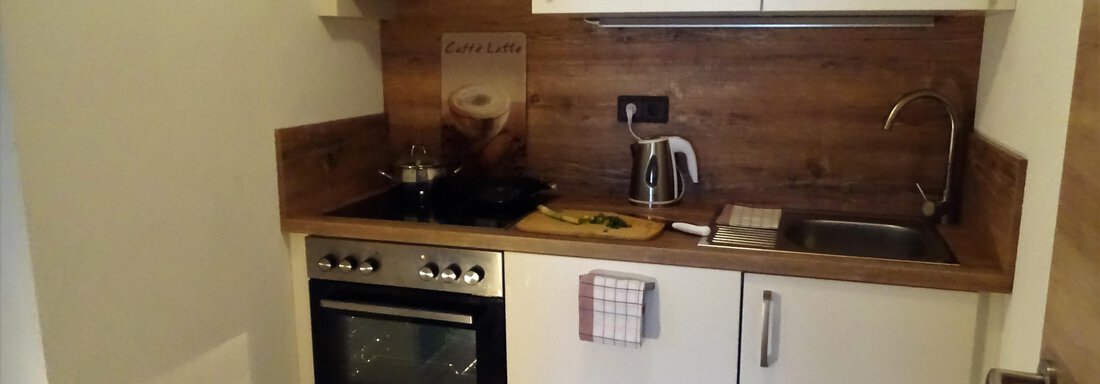 A small kitchen with a modern stove, kettle, and wooden shelf. The walls are bright and the furniture is in neutral colors. - Haus Alpenstern - Sölden