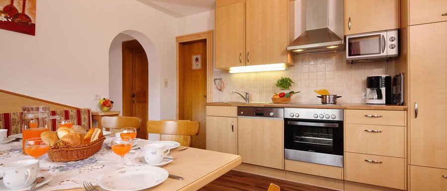 Wohnküche A modern kitchen with wooden furniture and stainless steel appliances. The table is lovingly set with breakfast and fresh rolls. - Haus Alpenstern - Sölden