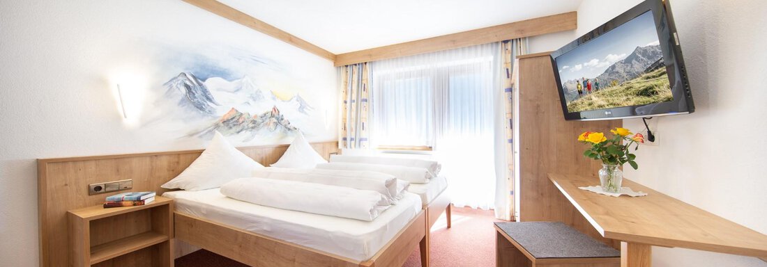A modern bedroom with two single beds and bright walls. A television and a small table with fresh flowers complement the decor. - Haus Alpenstern - Sölden