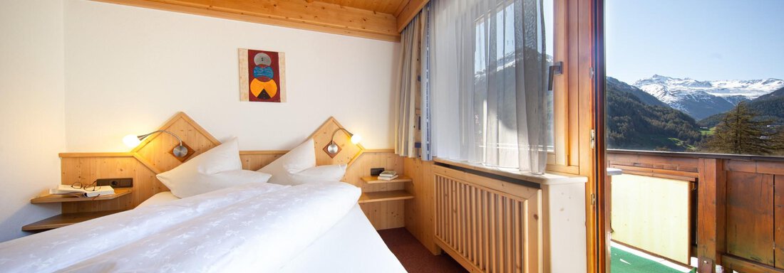 A cozy bedroom with a wooden ceiling and two beds. Large windows offer a view of the mountains. - Haus Alpenstern - Sölden