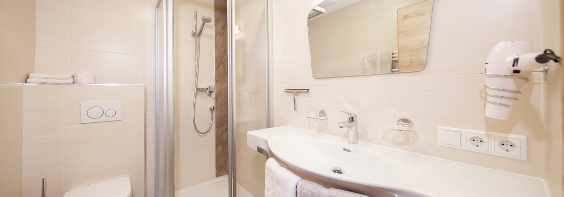 A modern bathroom with a shower cubicle, sink, and a toilet. The walls are bright, and the fixtures are elegant and functional. - Haus Alpenstern - Sölden