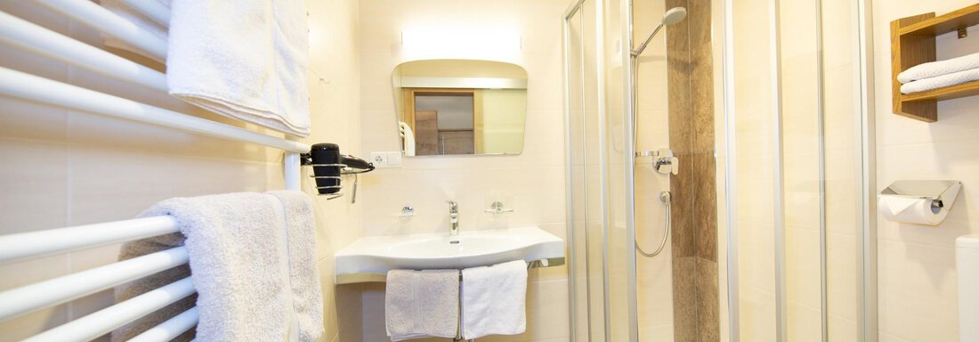 A modern bathroom with a shower, sink, and towels. The walls are bright, and the furnishings are stylish and functional. - Haus Alpenstern - Sölden