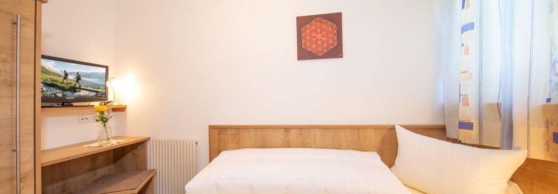 A cozy bedroom with a wooden bed and a television. Large windows let in plenty of light and create a friendly atmosphere. - Haus Alpenstern - Sölden