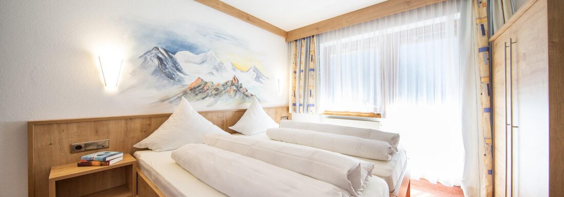A bright bedroom with two single beds and cozy wooden paneling. Large windows provide plenty of daylight and a pleasant atmosphere. - Haus Alpenstern - Sölden