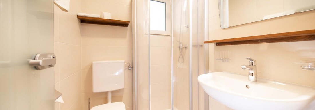A modern bathroom with a shower, a sink, and a toilet. The walls are light and the decor is simple and functional. - Haus Alpenstern - Sölden