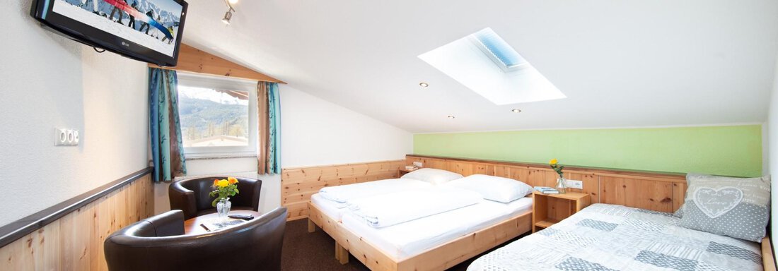 A cozy room with two beds and a television on the wall. The decor is bright and inviting, with a small table and chairs. - Haus Alpenstern - Sölden