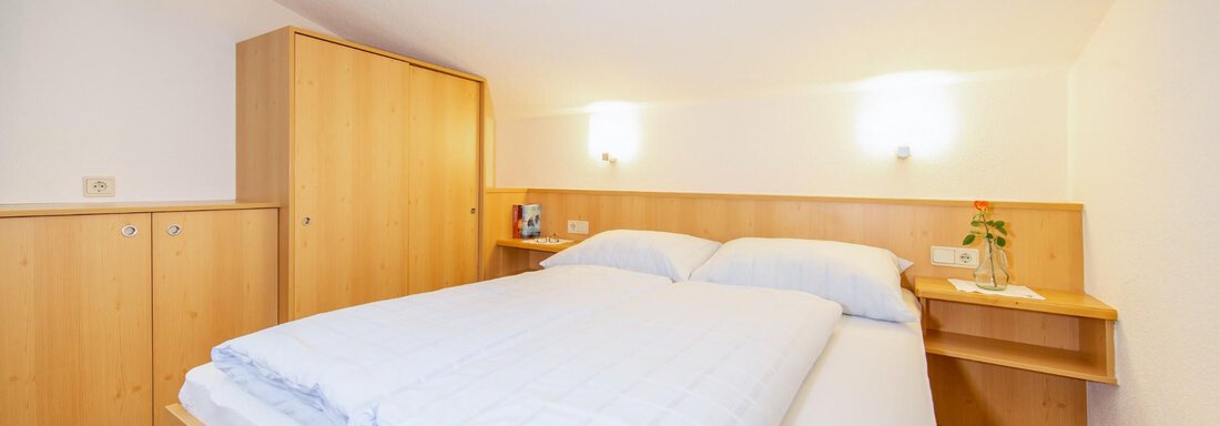 A simple bedroom with a double bed and wooden shelves. The walls are bright and the room feels cozy and tidy. - Haus Alpenstern - Sölden