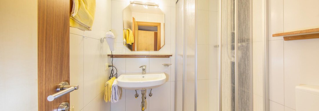 A modern bathroom with a shower, a sink, and bright tiles. Yellow towels and a rug add color to the space. - Haus Alpenstern - Sölden