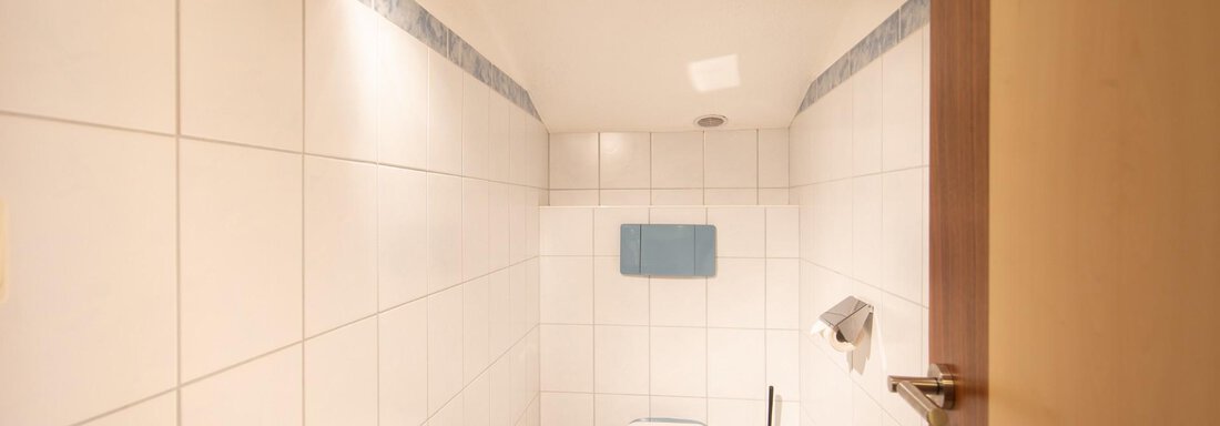 A modern bathroom with white tiles and a toilet. The walls are designed in a simple and minimalist style. - Haus Alpenstern - Sölden